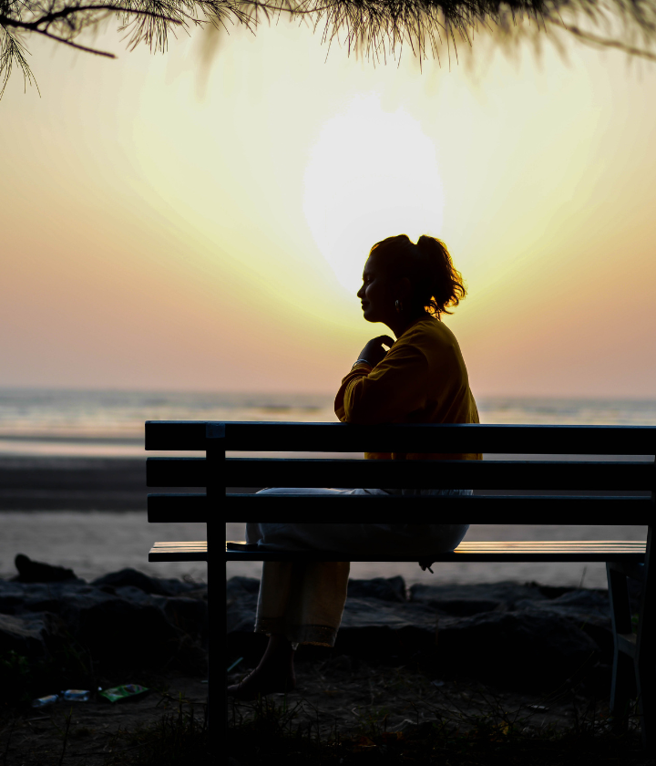 Woman sitting alone on bench facing ocean