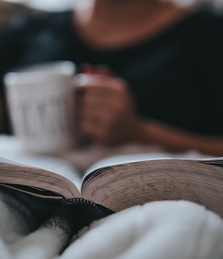 person in bed reading with a cup of tea